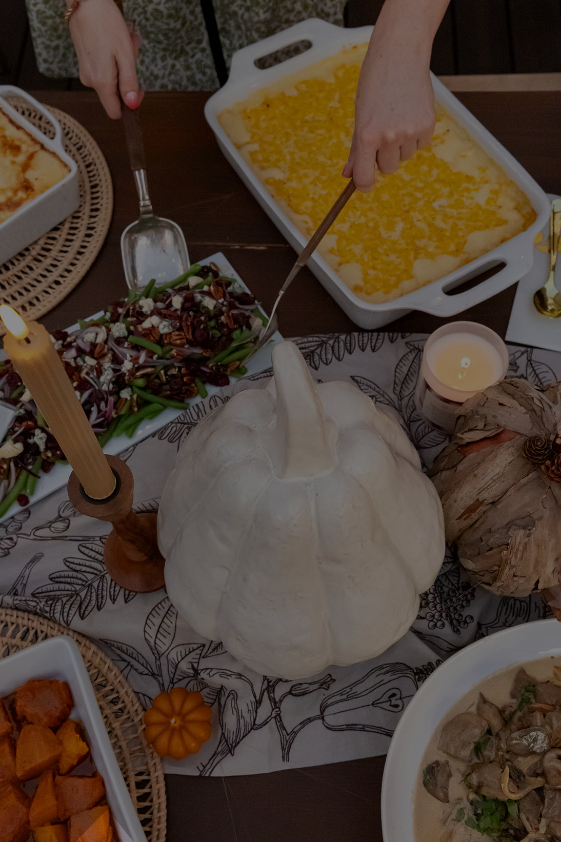 Dessert table with pumpkin, candles, and various dishes including a casserole.